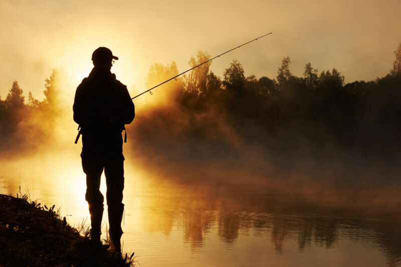 fisher,man,fishing,with,spinning,rod,on,a,river,bank